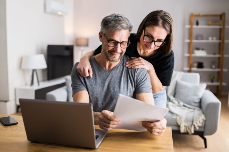 A couple completing their taxes at a desk in front of a laptop.