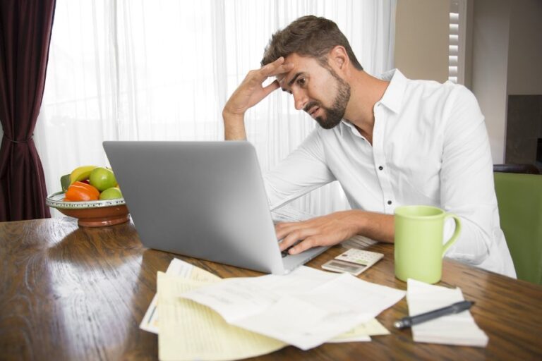 A stressed-out man doing his taxes on a laptop.